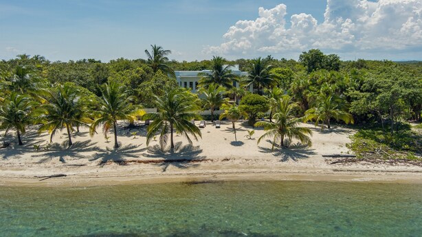 Una propiedad frente a la playa con un edificio grande rodeado de palmeras y aguas turquesas cristalinas.