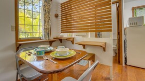 Una cucina funzionale con piani in legno, un tavolo da pranzo con sedie, una finestra con tende e un forno a microonde su un mobile bianco.