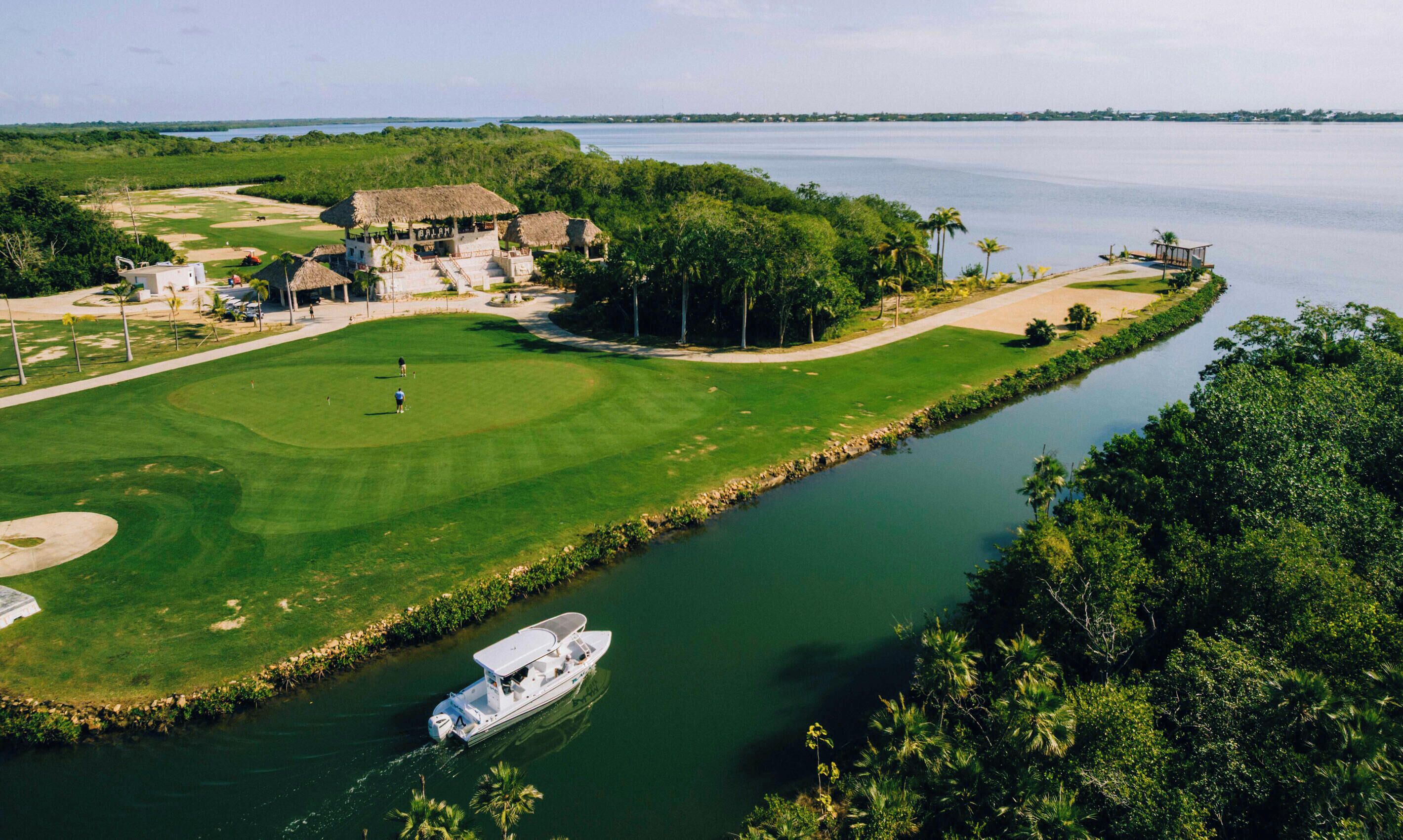 A golf course with a water body, a boat, and a building with a thatched roof.