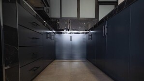 Un couloir étroit, doté de meubles et de tiroirs sombres, d’un évier central et d’un sol carrelé.