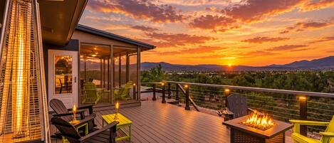 Terraza con asientos al aire libre y una chimenea, con vistas a un paisaje de montañas y un atardecer.