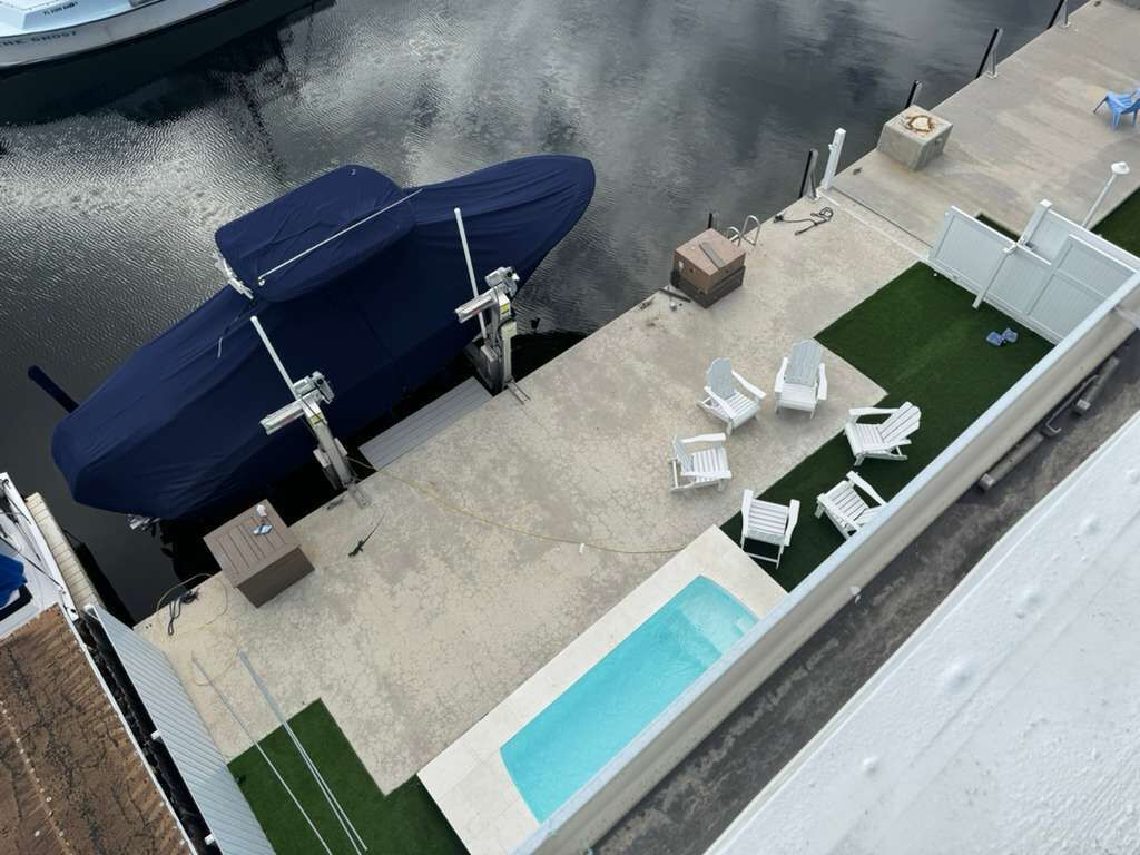 An aerial view of a rooftop pool area with a covered boat, lounge chairs, and a small deck.