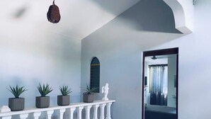 A hallway with a white balustrade, potted plants, a hanging light fixture, and a doorway leading to a room with a bed and curtains. - HOTEL CASA VERDE (Troncones)