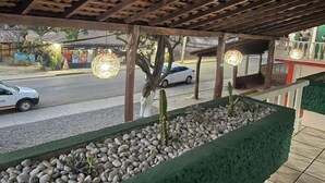 A covered outdoor area with a wooden ceiling, a green planter with cacti and pebbles, and a street view with cars and buildings in the background. - HOTEL CASA VERDE (Troncones)