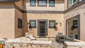 Un patio de piedra con mobiliario exterior, una puerta y plantas colgantes.