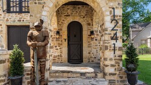 Un edificio de piedra con una entrada rústica, una placa con un número y una estatua de un caballero.