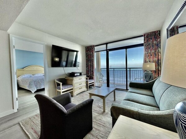 Habitación de hotel con cama, televisión, escritorio, sofá y balcón con vistas.