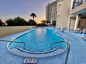Una piscina con indicador de profundidad de 3 pies, sillas de descanso y un edificio alto al fondo.