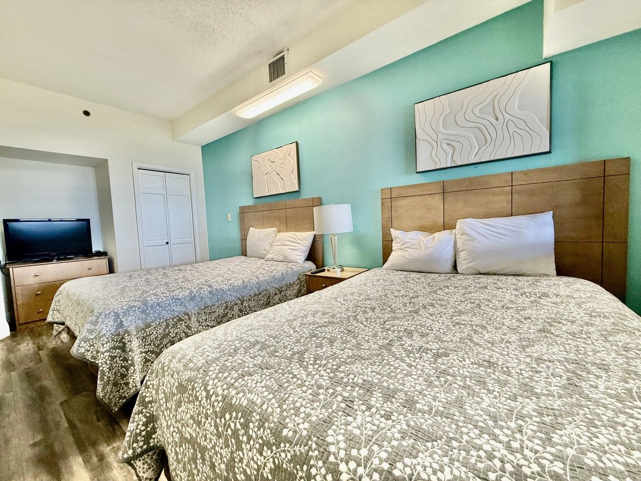 A hotel room with two beds, a television, and artwork on the walls.