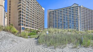 Et strandhotel med flere etager, en sti af sand ned til stranden og et skilt, der angiver adgang til stranden.