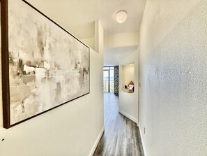 A hallway with a large abstract painting on the left, a textured wall on the right, and a view into a room with a window and curtains. - Tropical Resort, Beachfront Condo with amazing oceanfront views!! 322 (North Myrtle Beach)
