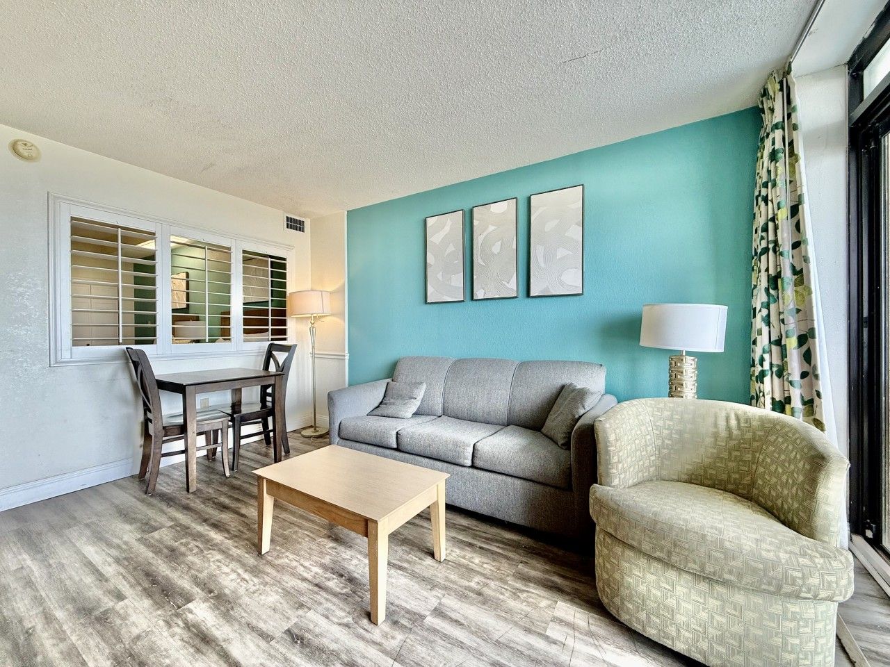 A living room with a sofa, armchair, coffee table, and a dining table with chairs.
