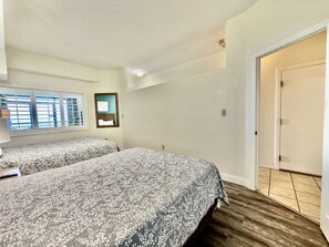 A bedroom with two beds, a window with blinds, a door, and a wooden floor. - Tropical Resort, Beachfront Condo with amazing oceanfront views!! 322 (North Myrtle Beach)