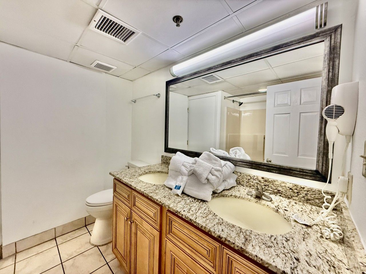 A bathroom with a granite countertop, two sinks, a mirror, a towel rack, and a hairdryer.