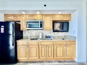 A kitchen with wooden cabinets, a black refrigerator, a microwave, a stove, and a flat-screen TV.