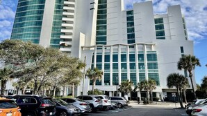 A modern hotel with a curved facade, multiple floors, and a parking lot in front. - Right next to family Kingdom! Oceanfront 1br full kitchen washer/dryer 1107 (Myrtle Beach)