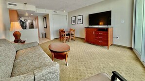 A hotel room with a living area featuring a sofa, a round coffee table, a TV, and a wooden cabinet. There is a dining table with chairs in the background. - Right next to family Kingdom! Oceanfront 1br full kitchen washer/dryer 1107 (Myrtle Beach)