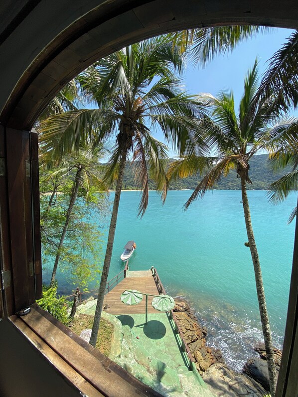 A view from a window overlooking a beach with palm trees, a dock, and a boat.