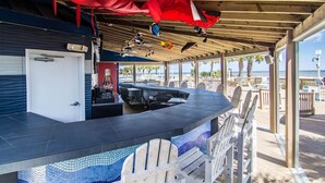 Un espace bar extérieur avec vue sur la piscine, un réfrigérateur à boissons Coca-Cola et un coin salon couvert avec des fauteuils Adirondack.