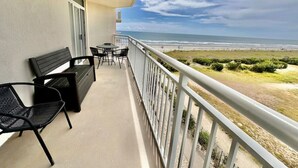 Un balcon avec vue sur la plage, un banc et une table avec des chaises.