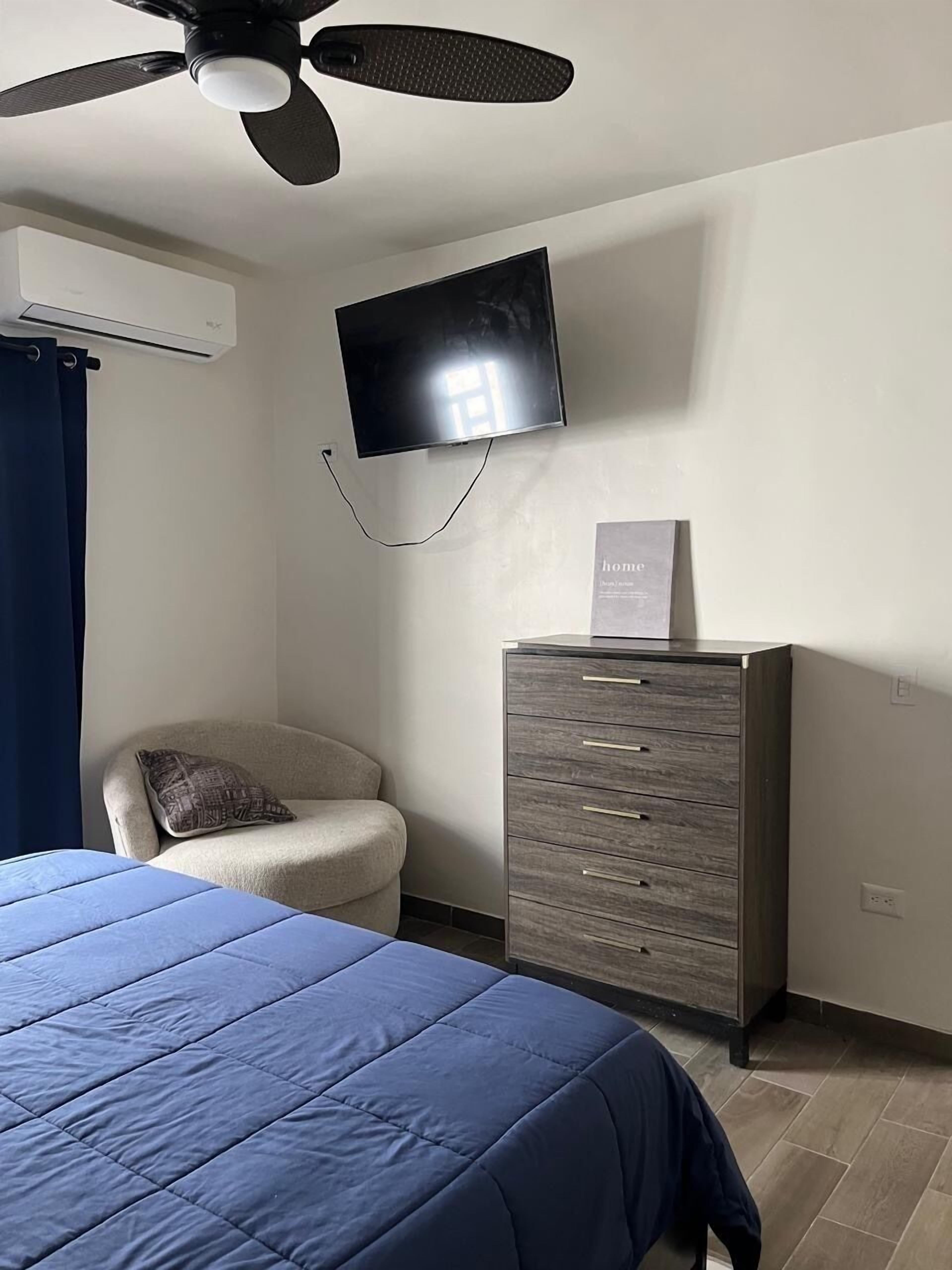 Une chambre à coucher comprenant un lit, une chaise, un téléviseur fixé au mur et un meuble.