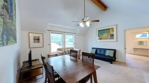A spacious living room with a wooden dining table, a sofa, and a ceiling fan. - The Buttercup Cottage (San Marcos)