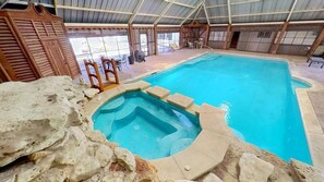 An indoor swimming pool with a hot tub, stone walls, and wooden furniture. - The Buttercup Cottage (San Marcos)