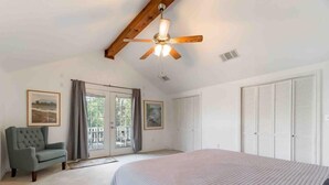 A bedroom with a large bed, a ceiling fan, a chair, and a view of the outdoors through a sliding door.