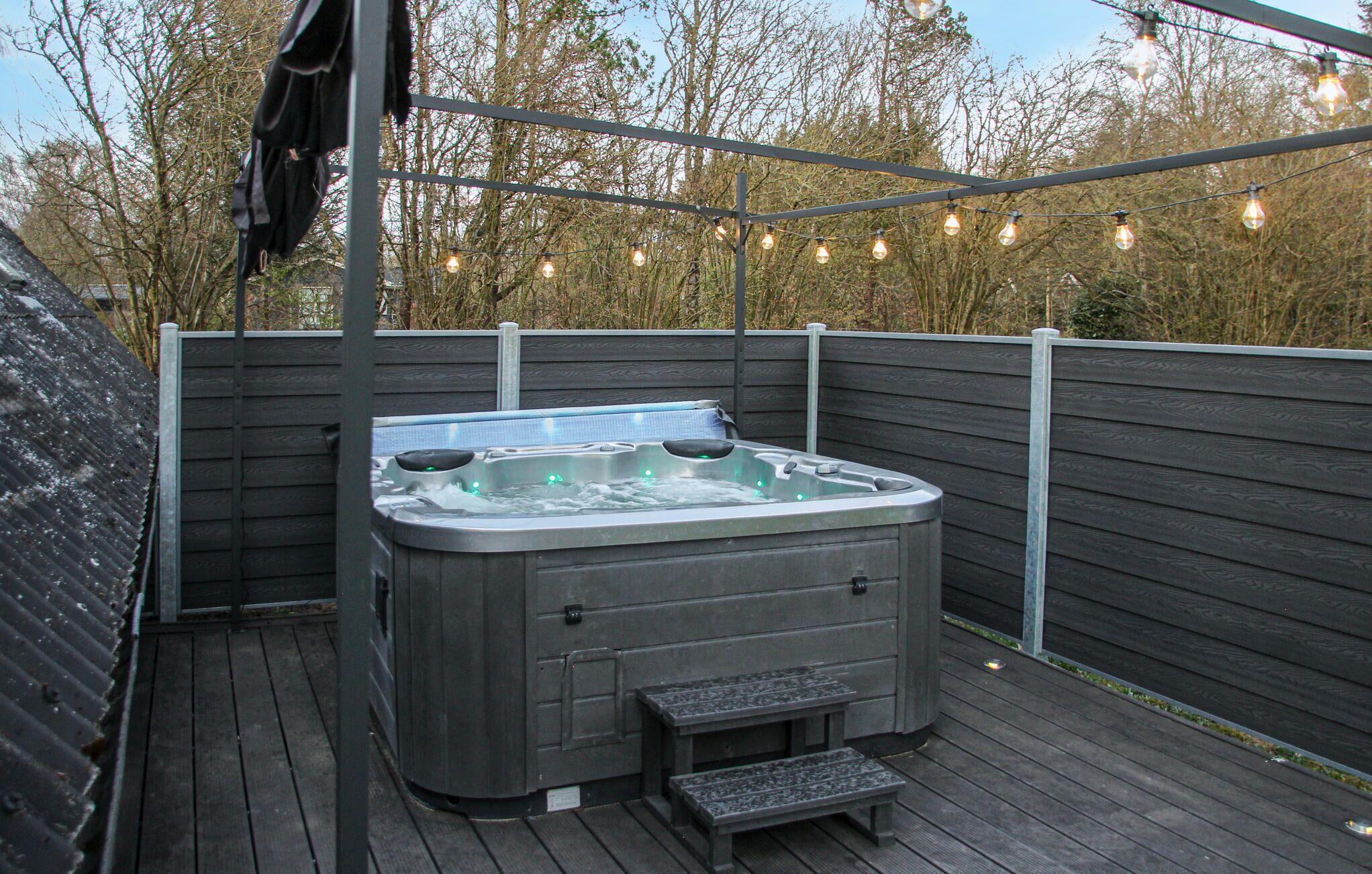 A hot tub on a wooden deck with a wooden fence and string lights in the background.
