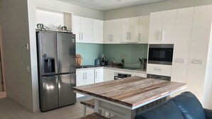 Eine moderne Küche mit weißen Schränken, einem Edelstahl-Kühlschrank, einem Holztisch und einer schwarzen Ledersofa.