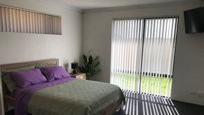 A bedroom with a bed, a nightstand, a lamp, a potted plant, and a sliding glass door leading to a balcony.