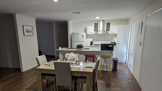 A modern kitchen with white cabinets, a central island, and a dining area with a wooden table and chairs.
