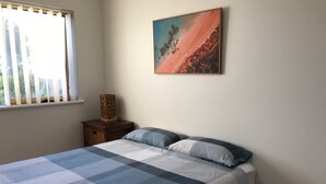 A bedroom with a large bed, a nightstand, a window with blinds, and a painting on the wall. - Marina Retreat Geraldton - Centrally Located in Garden Setting (Beresford)