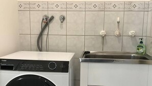 A compact laundry room with a front-loading washer and dryer, a small sink, and a cabinet. - Marina Retreat Geraldton - Centrally Located in Garden Setting (Beresford)
