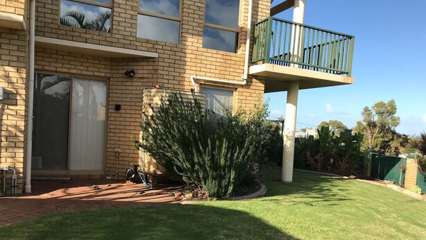 A two-story building with a brick facade, a balcony with green railings, and a well-maintained lawn. - Marina Retreat Geraldton - Centrally Located in Garden Setting (Beresford)