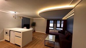 Un appartement moderne comprenant une cuisine, un coin repas et un salon. Il est doté d’un plancher en bois, d’un téléviseur à écran plat, d’une table à manger et d’un canapé.