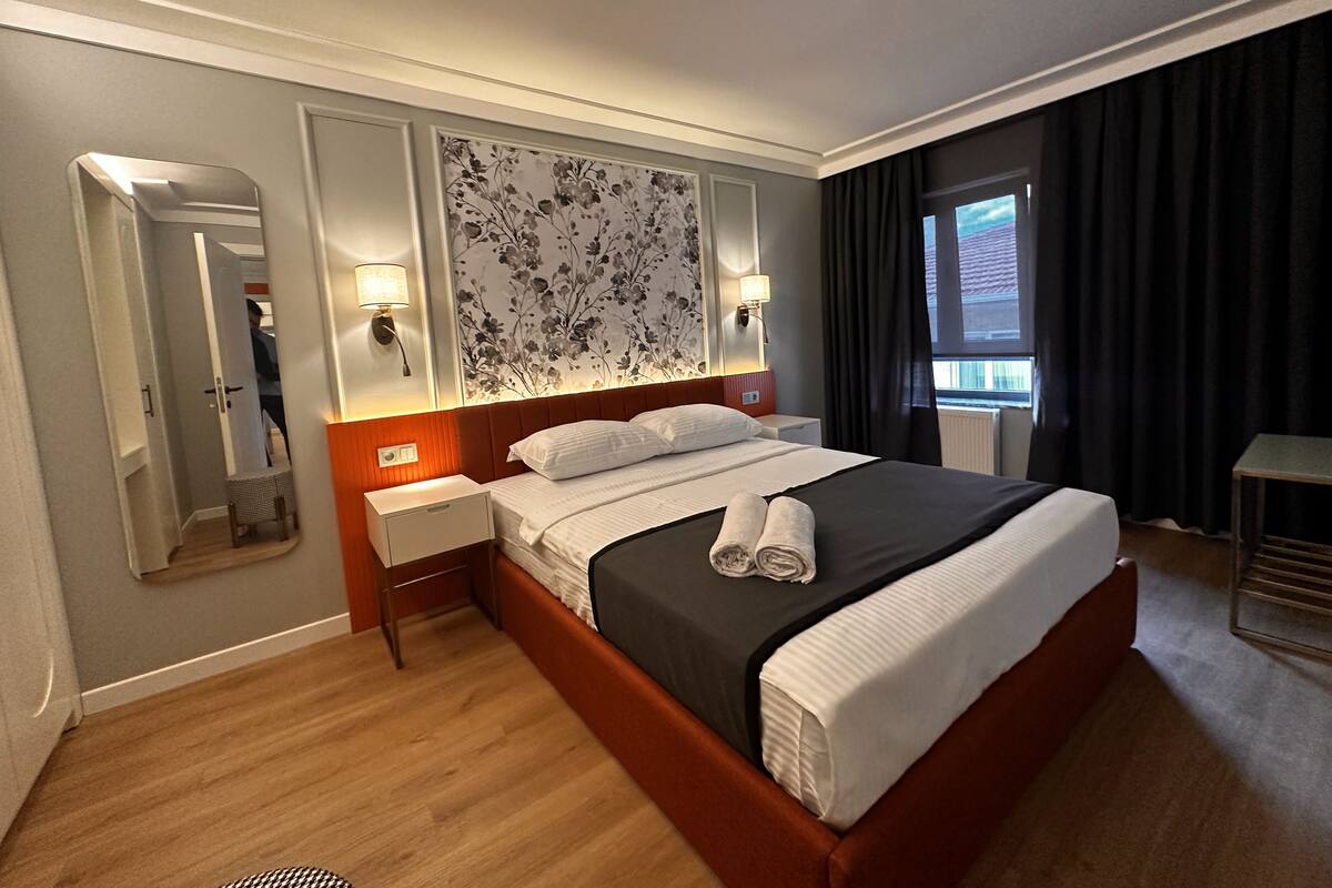 A hotel room with a large bed, a nightstand, a mirror, and a window with curtains.