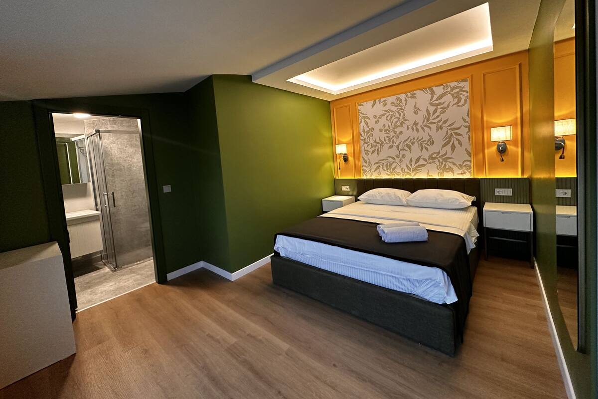 A modern hotel room with a bed, bedside tables, a shower, and a green accent wall.