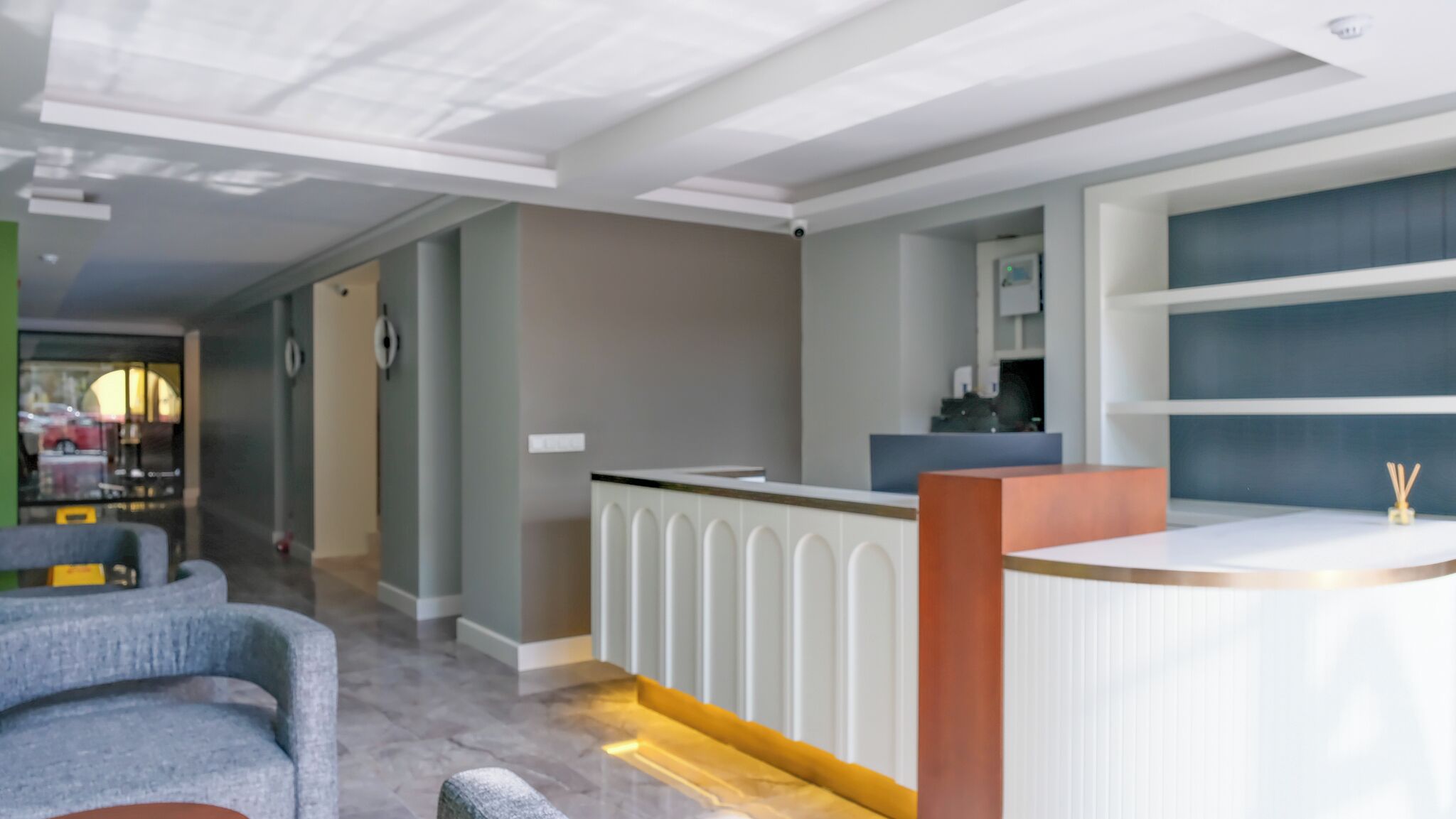 A modern reception area with a white reception desk, grey seating, and a view of the street outside.