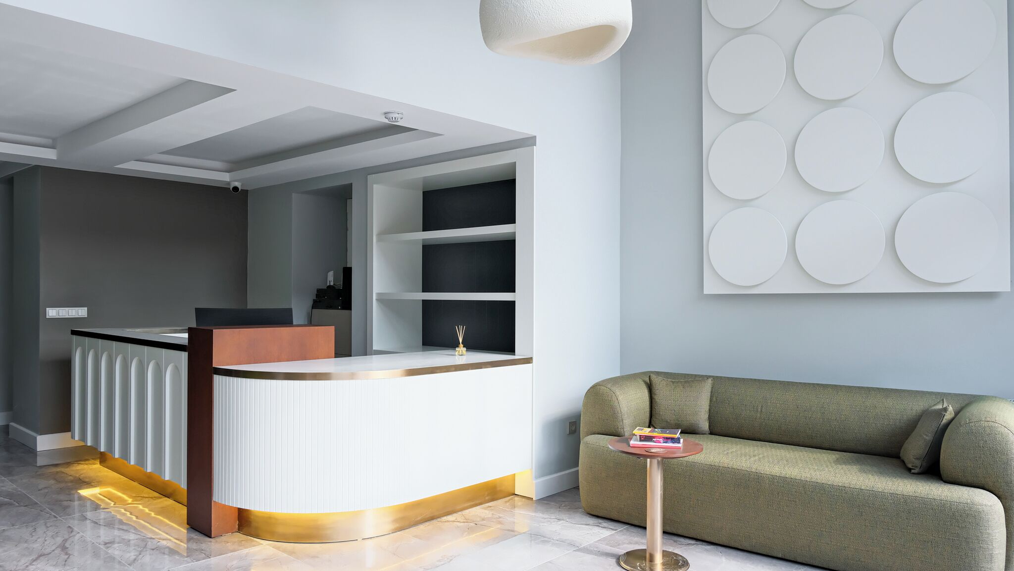 A modern reception area with a curved counter, a green sofa, and a decorative wall panel.