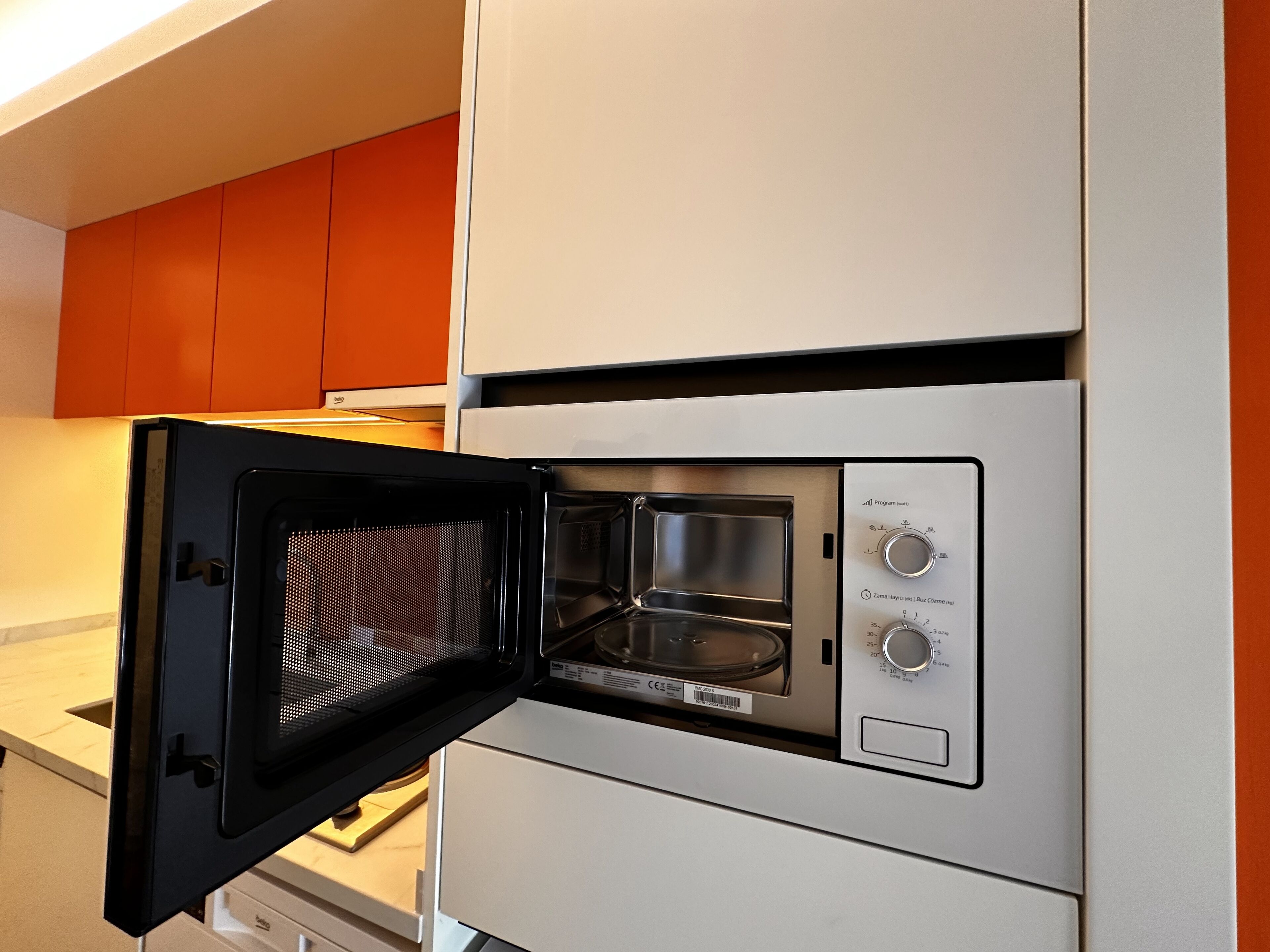 Un four à micro-ondes compact, encastré dans un meuble de cuisine blanc, avec un panneau de commande situé sur le côté droit.