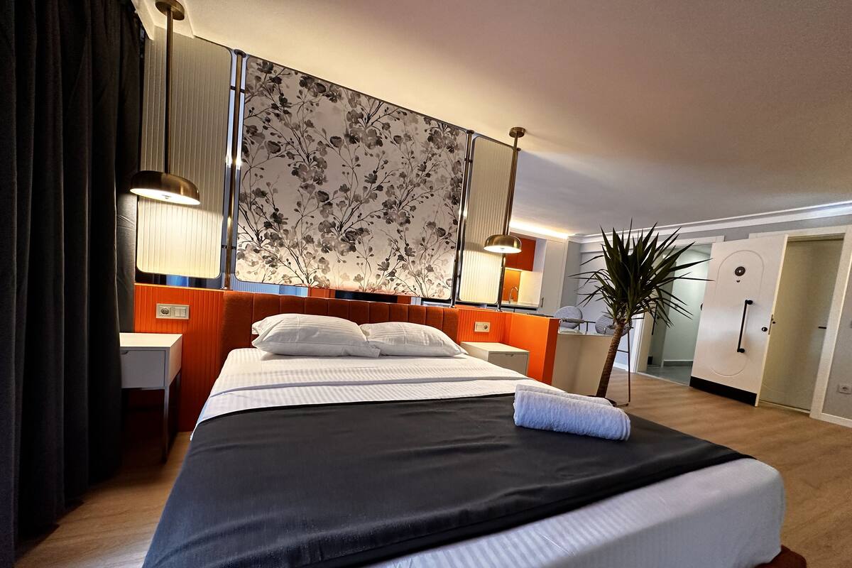 A hotel room with a large bed, bedside tables, a mirror, a plant, and a wardrobe.