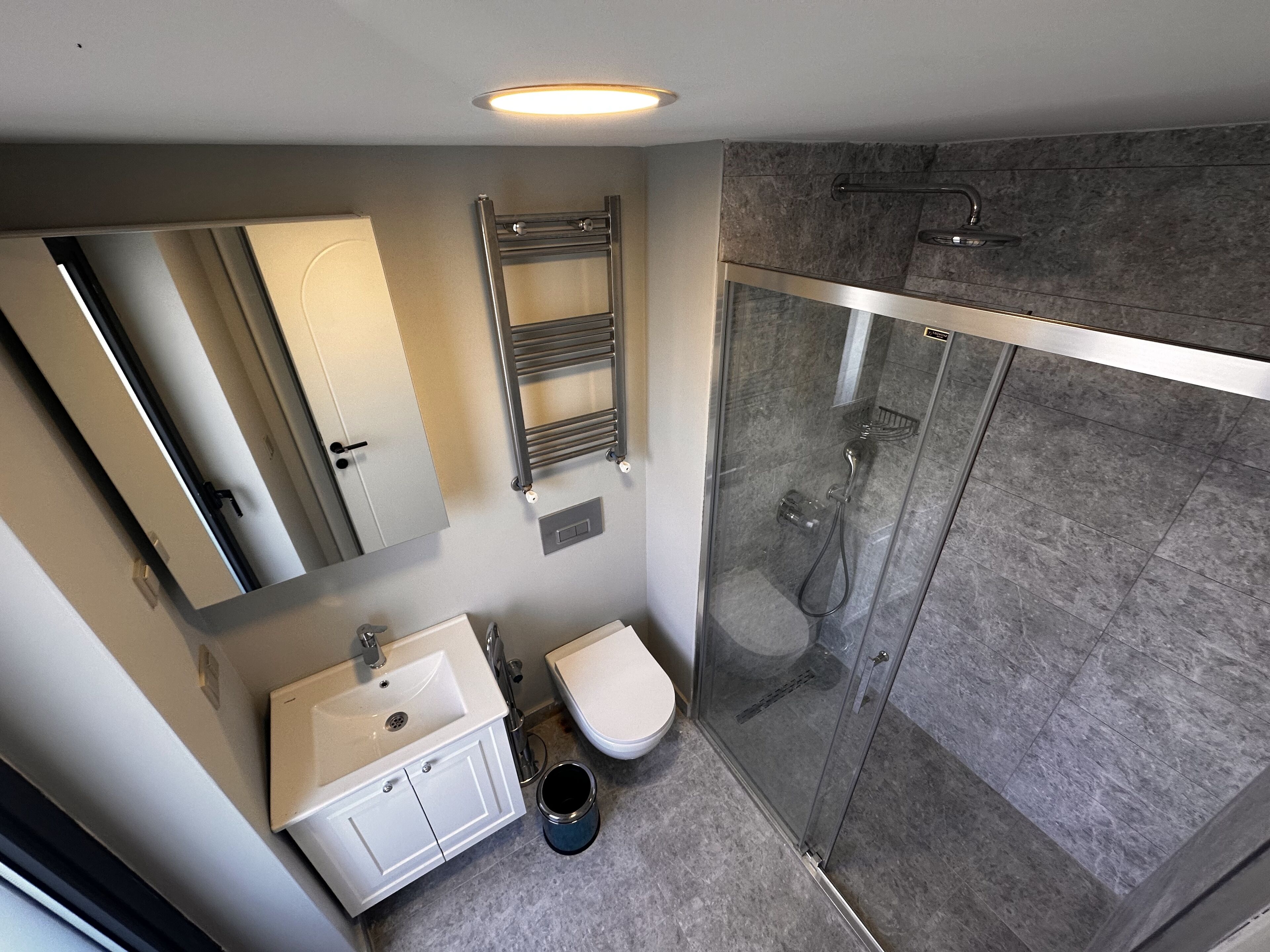 Un baño moderno con cabina de ducha de vidrio, un lavabo blanco y un inodoro.