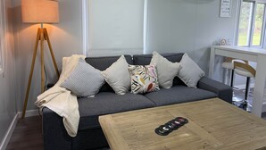 A modern living room with a grey sofa, striped pillows, a wooden coffee table, and a floor lamp. - The Bower (Paynes Crossing)