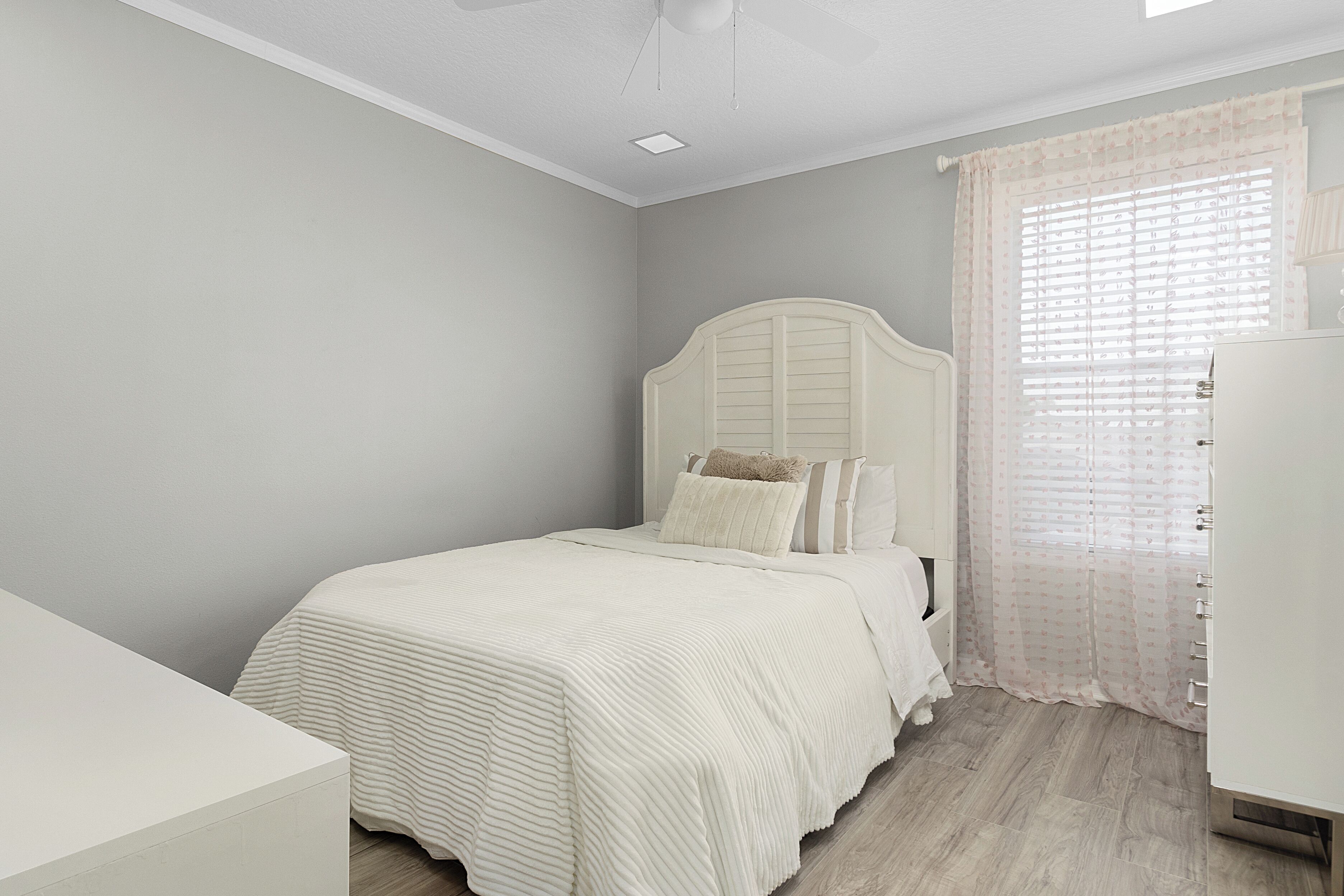 Une chambre à coucher avec un lit, une table de chevet, une commode et une fenêtre avec des rideaux.