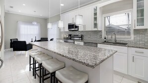 Una cocina moderna con armarios blancos, encimera de granito y taburetes de bar.