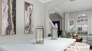 Un comedor amplio con una larga mesa blanca, dos candelabros de vidrio y una lámpara moderna.