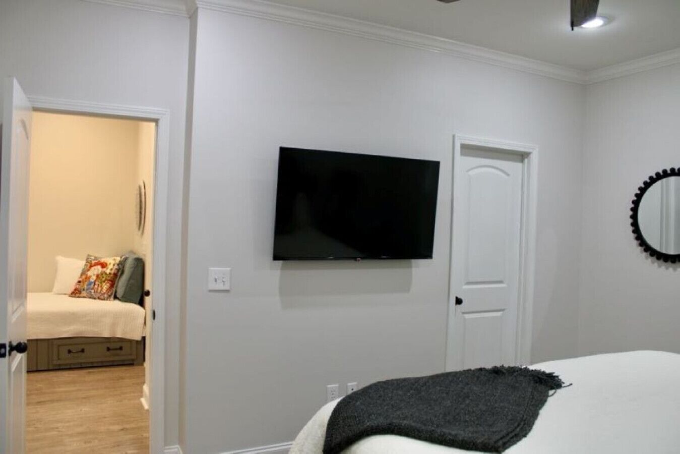 Um quarto com uma cama, televisão fixada na parede, uma porta e um espelho.