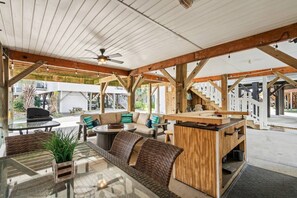 An outdoor patio area with a wooden pergola, seating, and a ceiling fan.