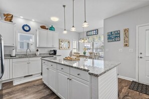 A kitchen with white cabinets, granite countertops, pendant lighting, and decorative wall art.